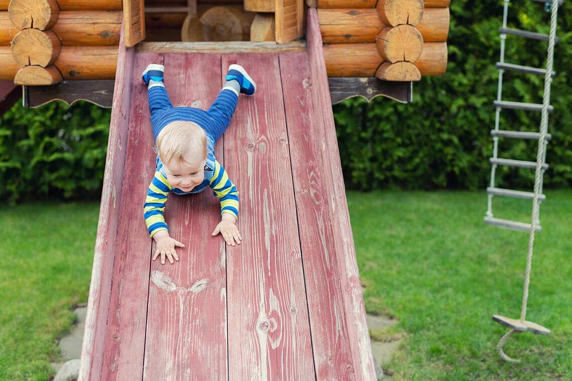 toddler going down a slide on backyard playhouse