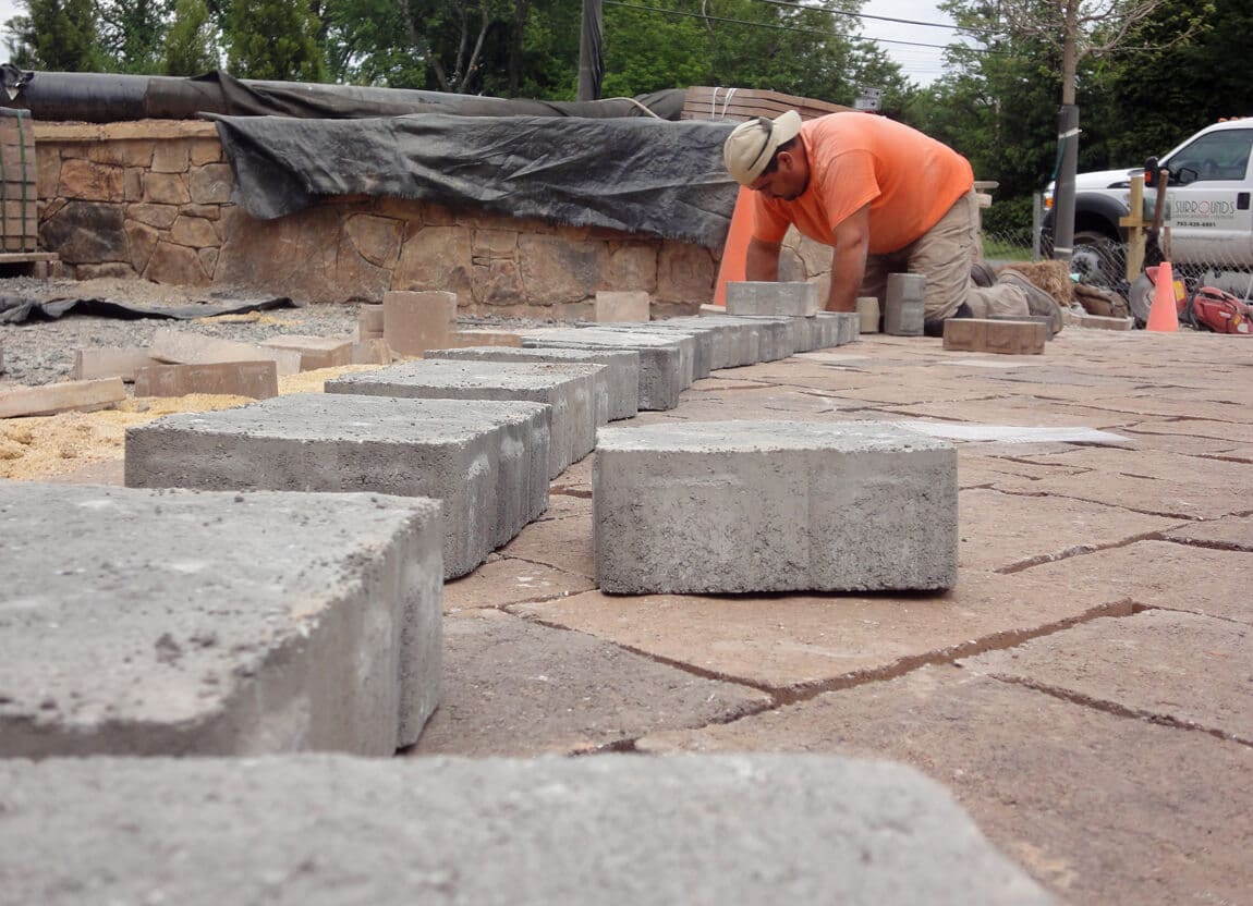 landscape construction tech lays pavers for new driveway